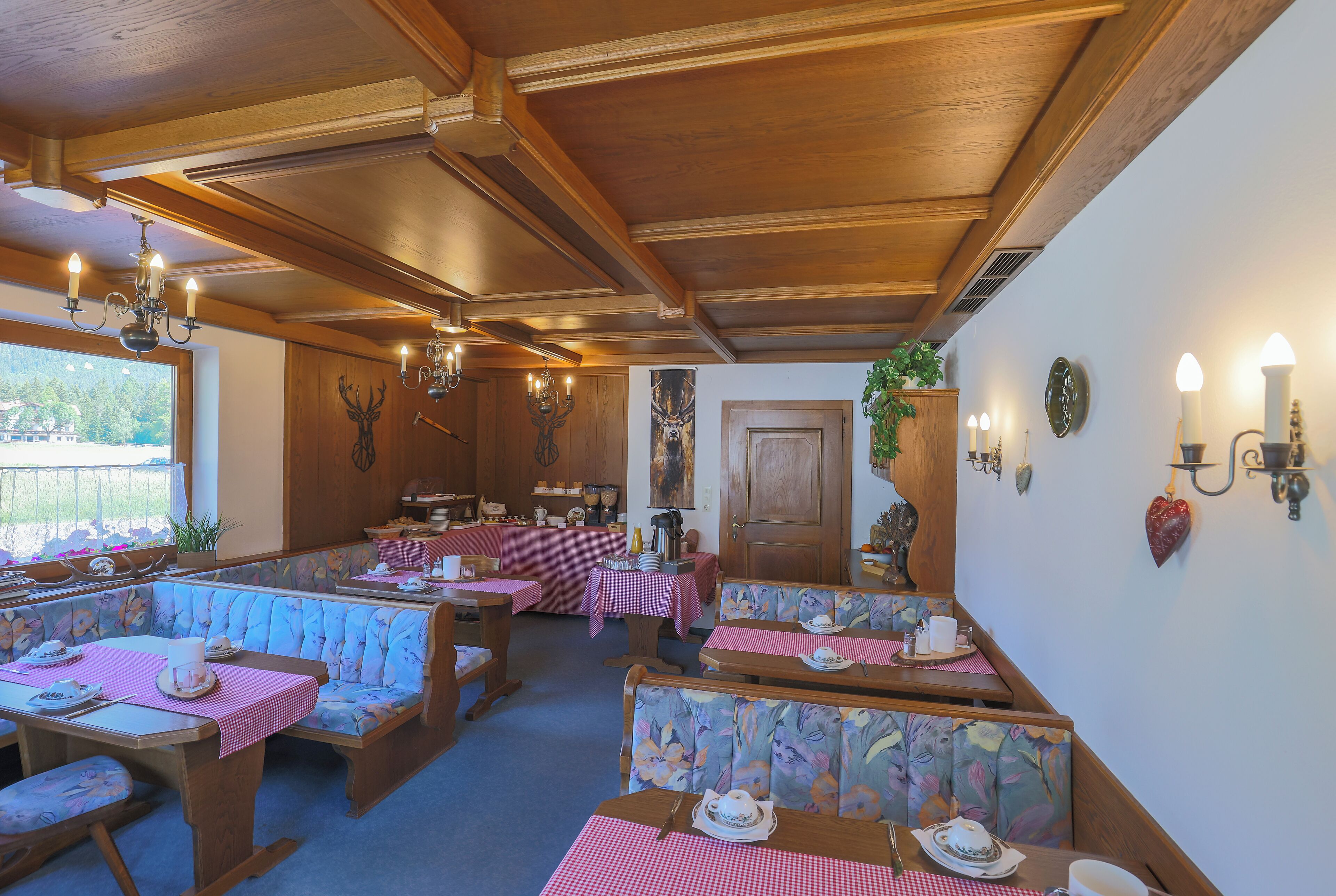 A restaurant with wooden booths and tables, a chandelier, and a view through a window.