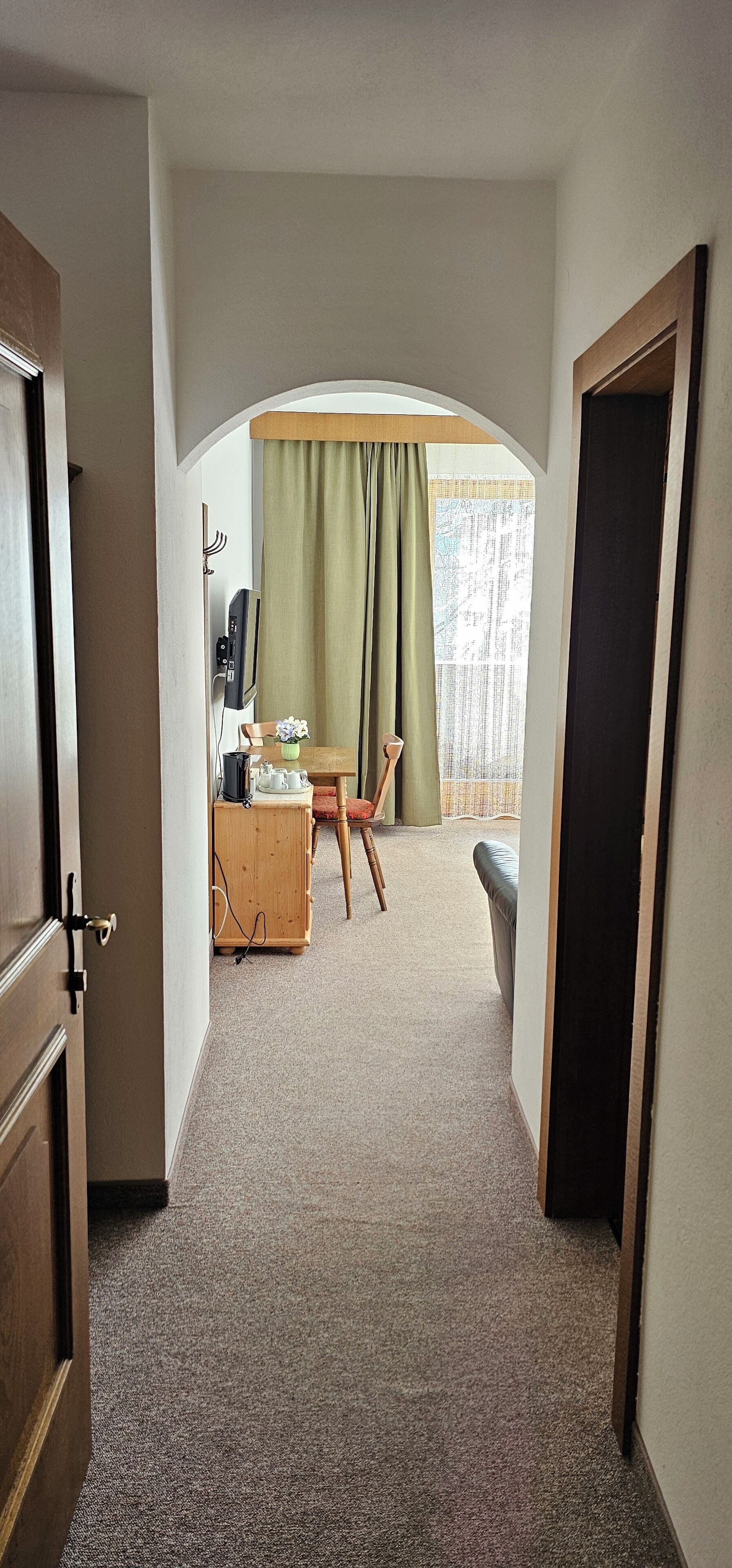 Una habitación de hotel con piso alfombrado, un escritorio de madera con una silla, un sofá y una ventana con cortinas.