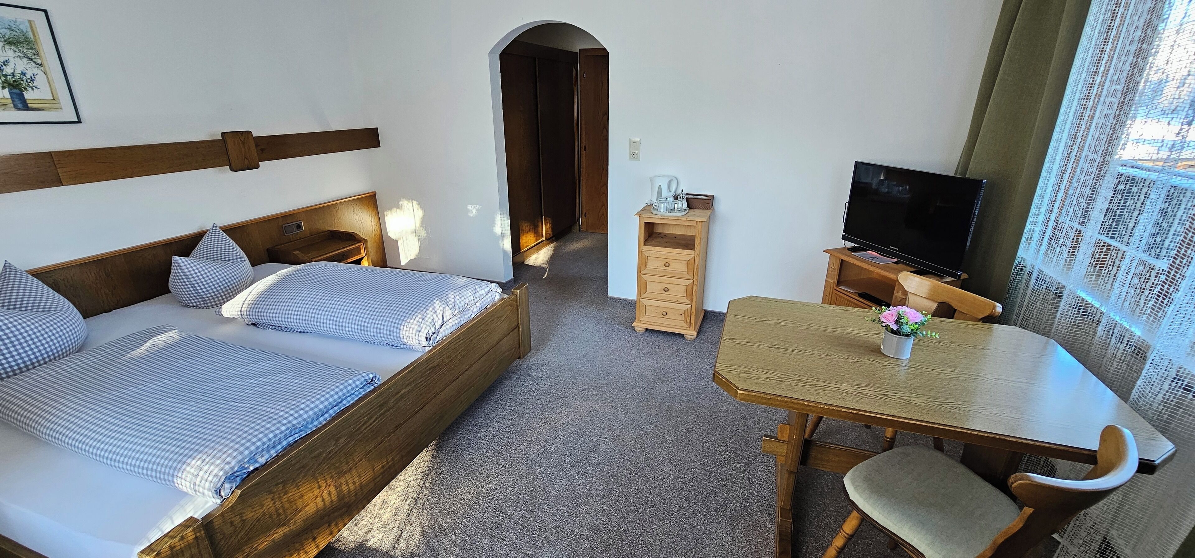 Une chambre à coucher avec un lit, un bureau en bois, une télévision et une petite table sur laquelle est posée une plante.