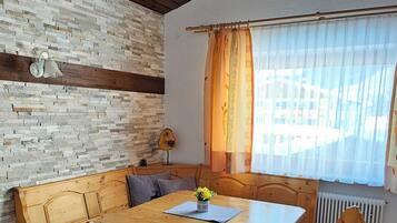 A wooden dining table with benches, a stone wall, and a window with curtains.