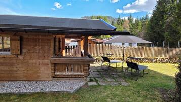 Una cabaña de madera con un porche, mobiliario exterior y vistas a una zona boscosa.