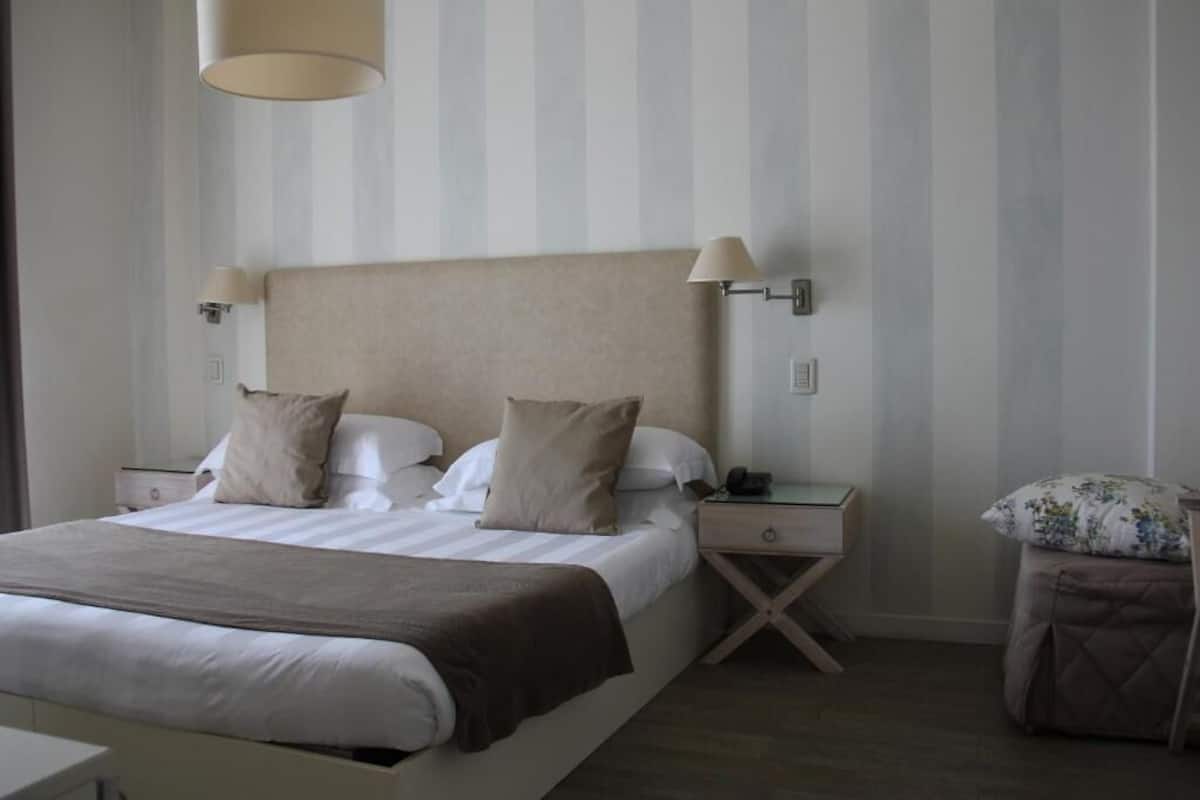 Een keurig opgemaakt hotelkamer met een groot bed, nachtkastjes en een bijzettafel.