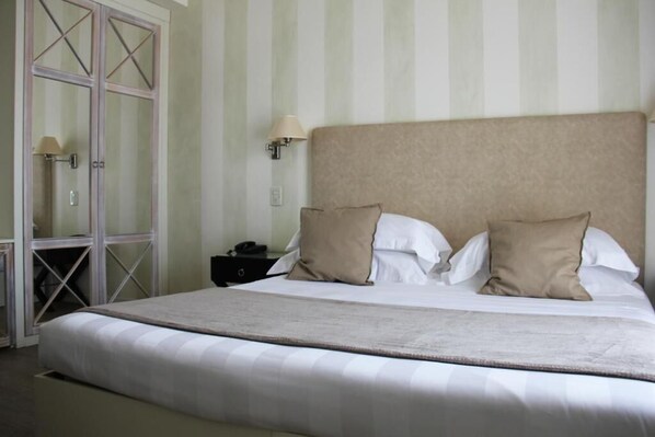 A neatly made bed with white linens and two beige pillows, a bedside lamp, and a nightstand with a phone.