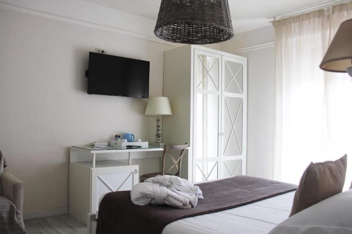 Een hotelkamer met een bed, een bureau met stoel, een televisietoestel, een kledingkast en een raam met gordijnen.