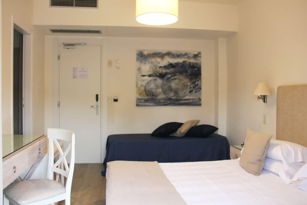Een hotelkamer met een bed, een stoel, een bureau en een schilderij aan de muur.