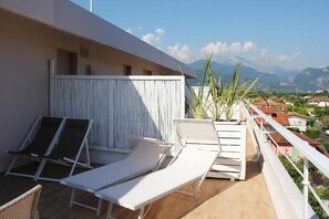 A balcony with white lounge chairs, a white fence, and a view of a town and mountains. - Hotel Bijou (Forte dei Marmi)