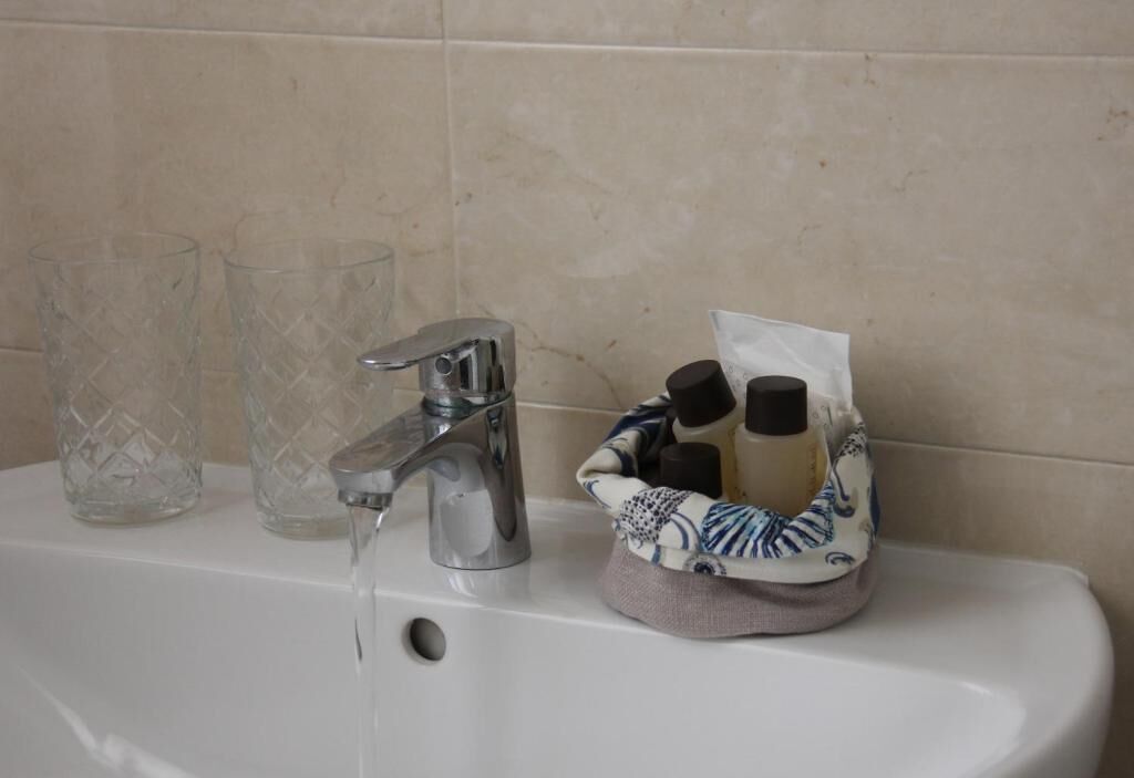 Un lavabo de salle de bain avec un robinet, deux verres transparents et un panier contenant des articles de toilette.