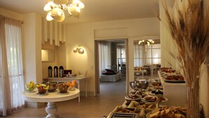 A buffet setup with various food items and a dining area with a chandelier.