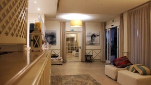A hotel lobby with a reception desk, a sofa with cushions, a patterned rug, and a door leading to a balcony.