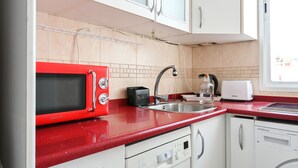 A kitchen with white cabinets, a red microwave, a toaster, and a dishwasher. - Cozy two-bedroom apartment in Delicias (Madrid)