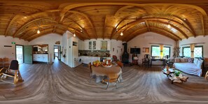 A spacious room with a high wooden ceiling, a dining area with a table and chairs, a sofa, and a fireplace.