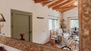 Een kamer met een houten plafond, een bed met metalen frame, een stoel en een klein houten krukje.