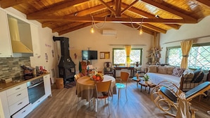 Een ruime woonkamer met houten plafond, een eettafel met stoelen, een bank en een televisie.