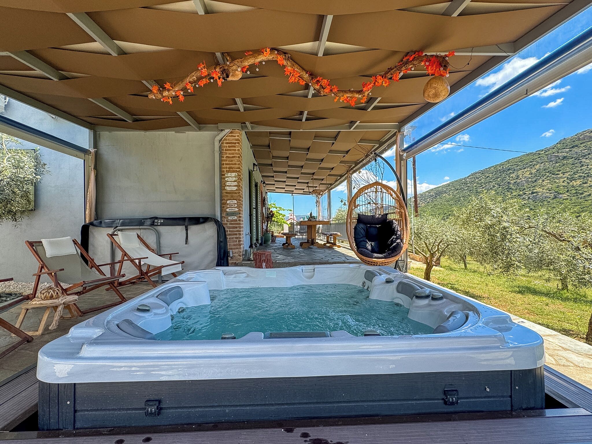 A hot tub with a view of a mountainous landscape, a covered seating area with chairs, and a hanging chair.