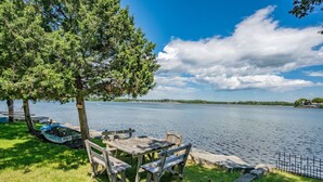 Järvenrantainen piknikalue, jossa on puinen pöytä ja penkit, ja jota ympäröivät puut ja nurmialue.