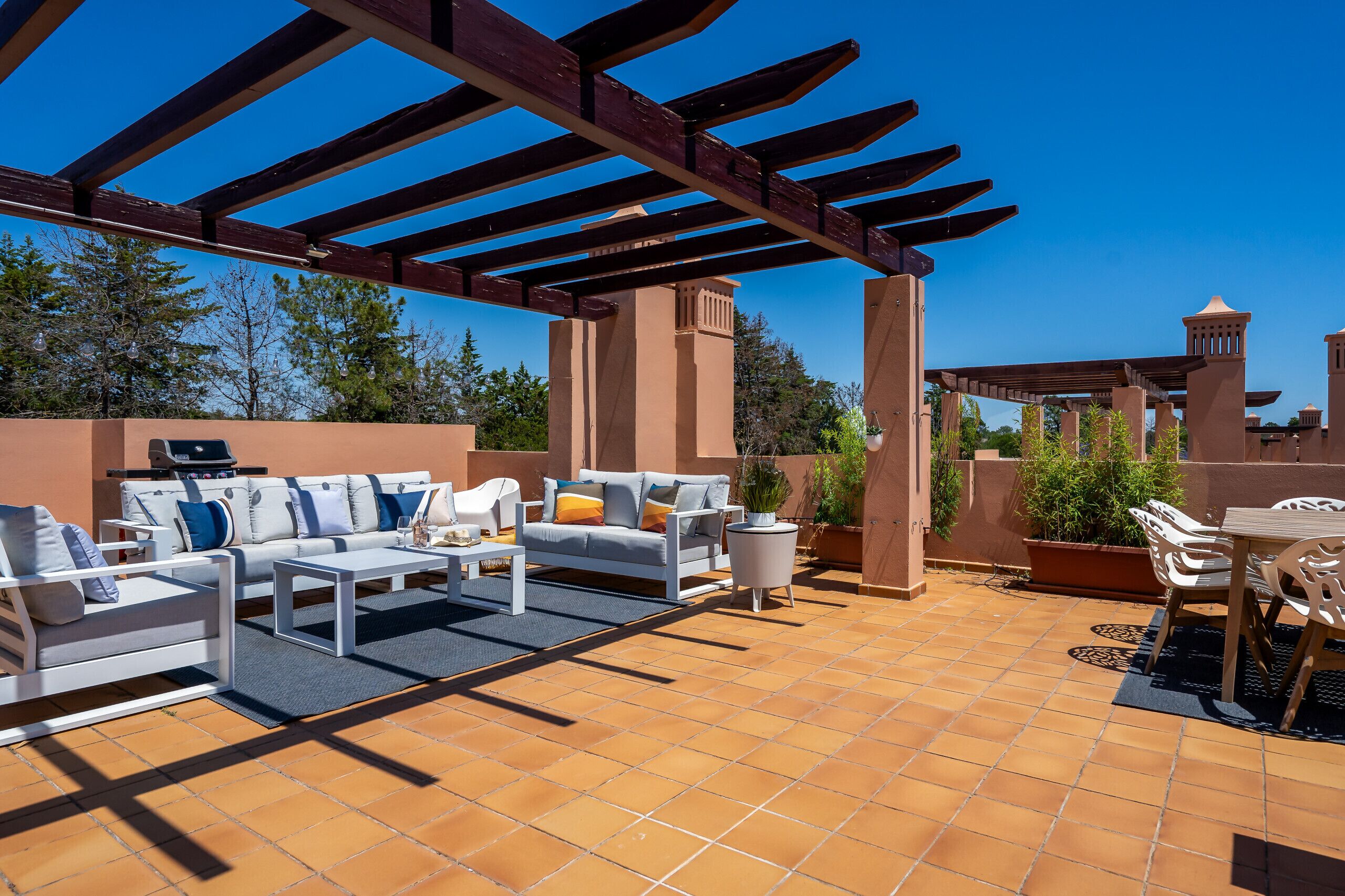 An outdoor patio with a pergola, seating area, and potted plants.