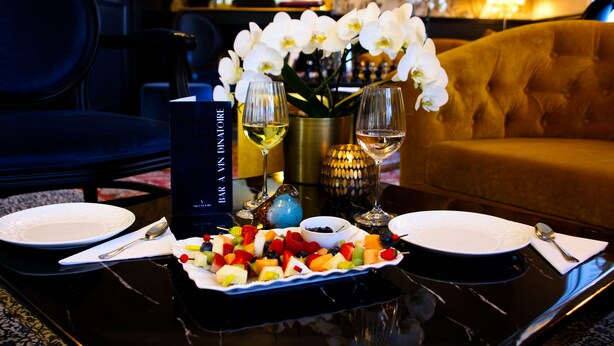 Ein Esstisch mit einer Obstplatte, zwei Weingläsern, einem Buch mit dem Titel 'BAR A VIN NATURE' und einer Vase mit weißen Blumen.