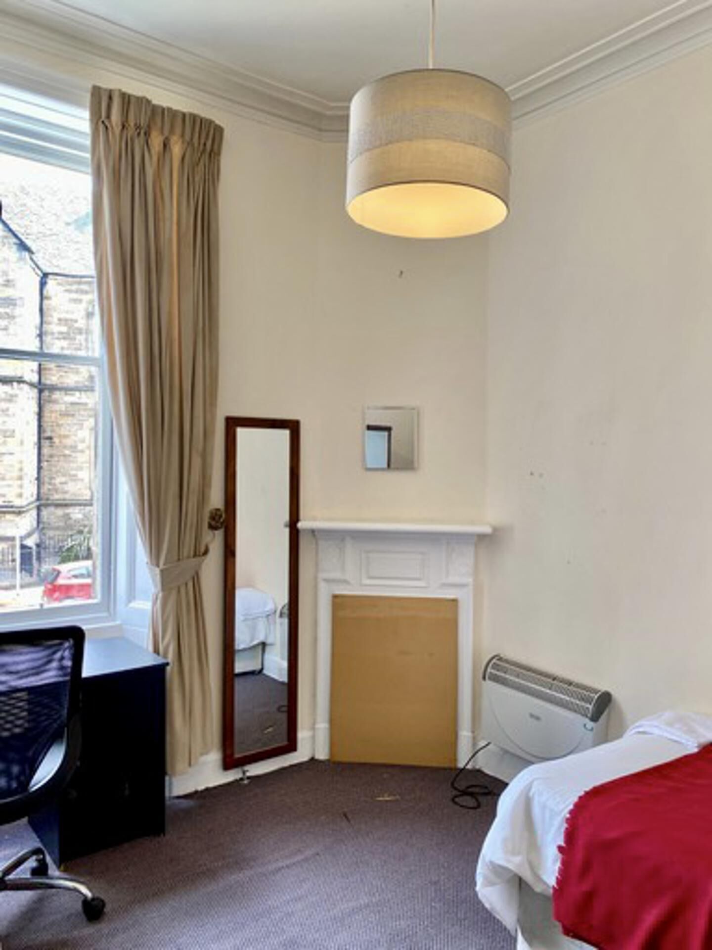 A hotel room with a large window, a mirror, a fireplace, a desk, and a bed.