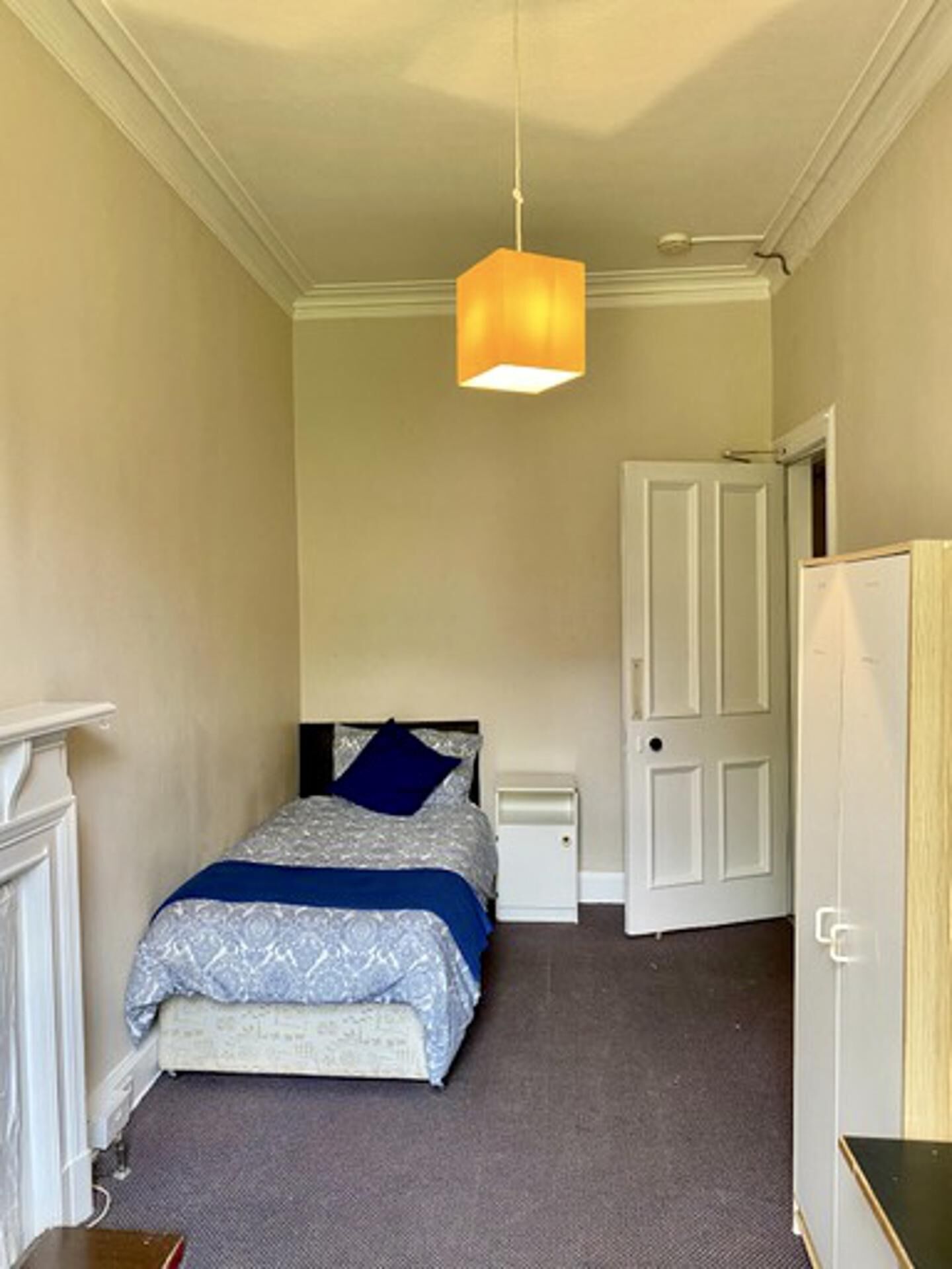 Un dormitorio con cama, mesitas de noche, lámpara colgante y una puerta.