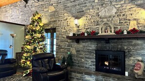 A cozy living room with a stone fireplace, a Christmas tree, and a leather sofa.