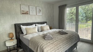 Un dormitorio con una cama grande, una mesita de noche con lámpara y vistas a la vegetación por la ventana.