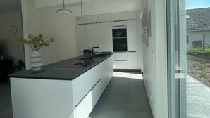 Una cocina moderna con una isla central, luces colgantes y vistas a través de un ventanal.