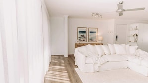 A modern living room with a white sectional sofa, a wooden floor, and a ceiling fan. - 'Key Point' - Tranquil Getaway - Mooloolaba (Mooloolaba)