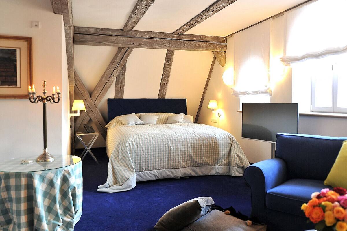 A bedroom with a bed, a blue sofa, a lamp, and a TV.