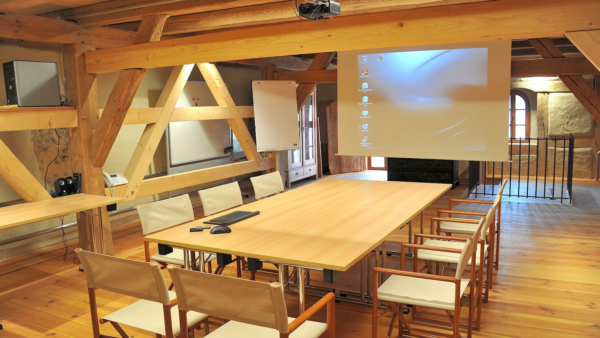 A conference room with a long table, several chairs, a projector screen, and a computer.