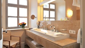 Un baño moderno con un lavamanos grande, dos grifos, un espejo y un florero con flores.