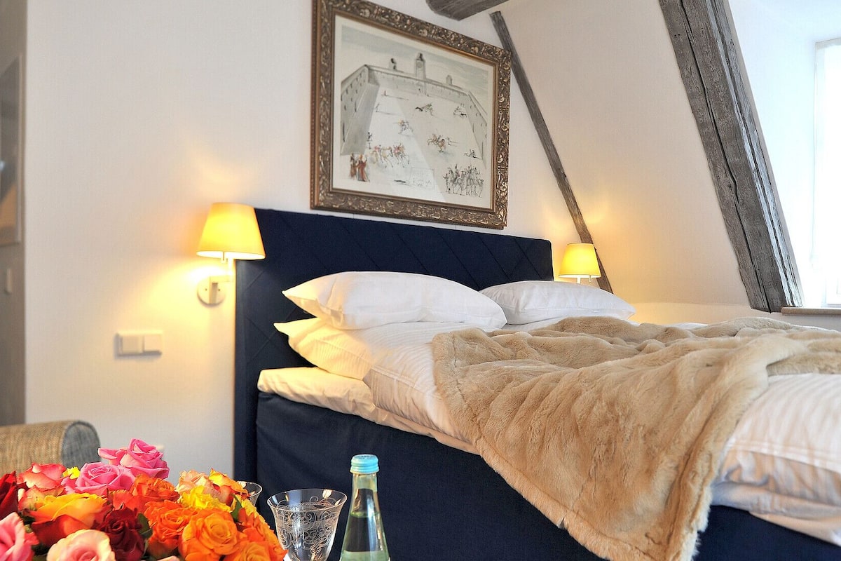 A neatly made bed with a dark headboard, two bedside lamps, and a framed picture above the bed.