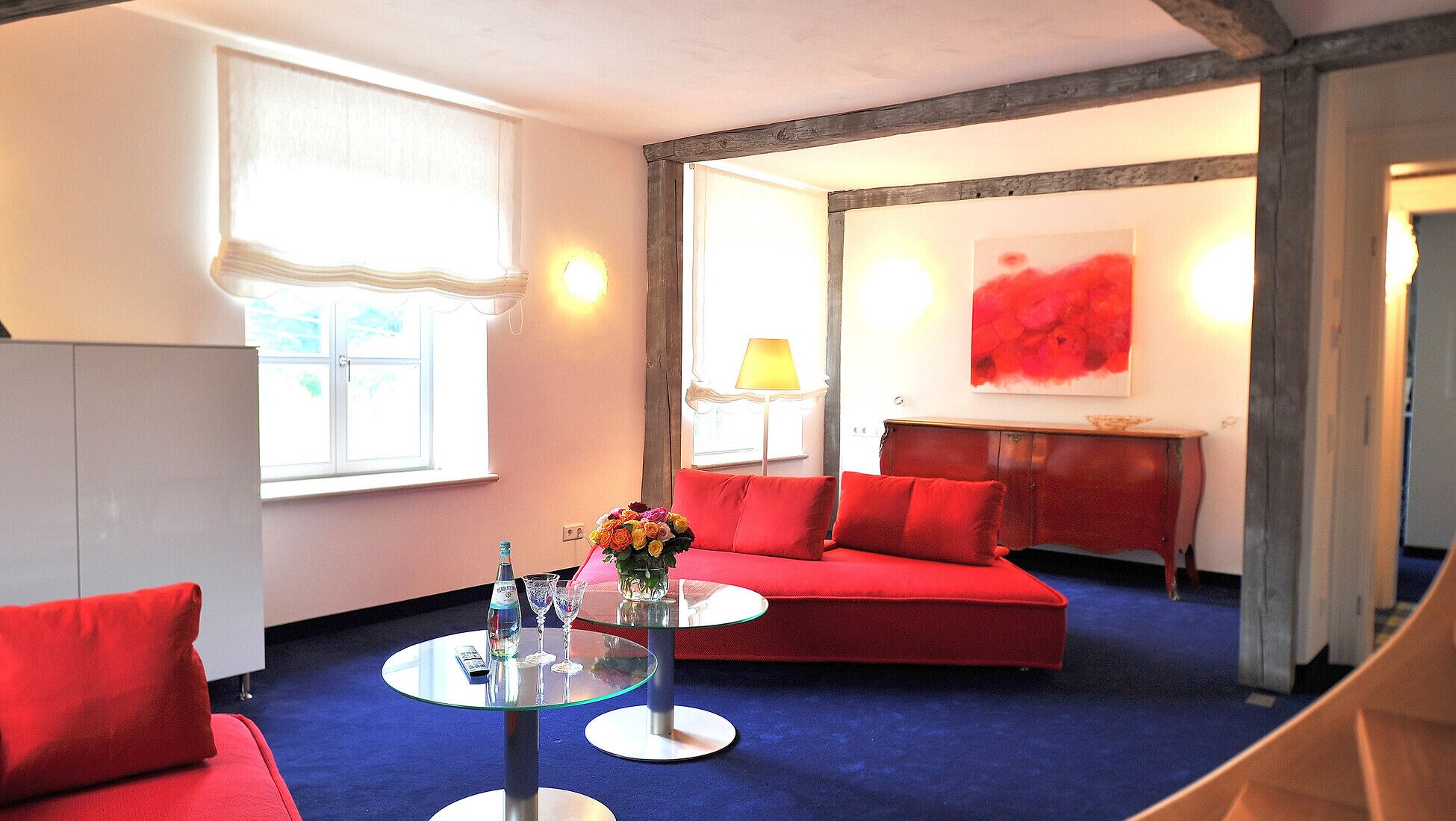 Una sala de estar moderna con un sofá rojo, una mesa de centro de vidrio y un jarrón de flores.