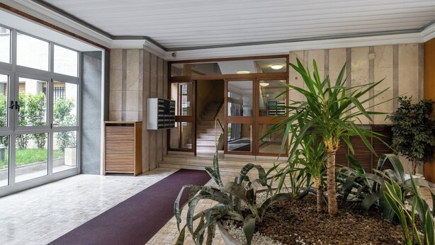A spacious lobby with large windows, a staircase, and a potted plant arrangement. - Appartamento vicino al Parco della Montagnola by Wonderful Italy (Bologna)