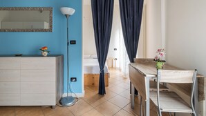 A room with a blue wall, a white cabinet, a wooden table, and a bed with dark curtains. - Appartamento vicino al Parco della Montagnola by Wonderful Italy (Bologna)