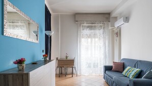 A modern living room with a blue accent wall, a wooden dining table, a sofa, and a large window with sheer curtains. - Appartamento vicino al Parco della Montagnola by Wonderful Italy (Bologna)