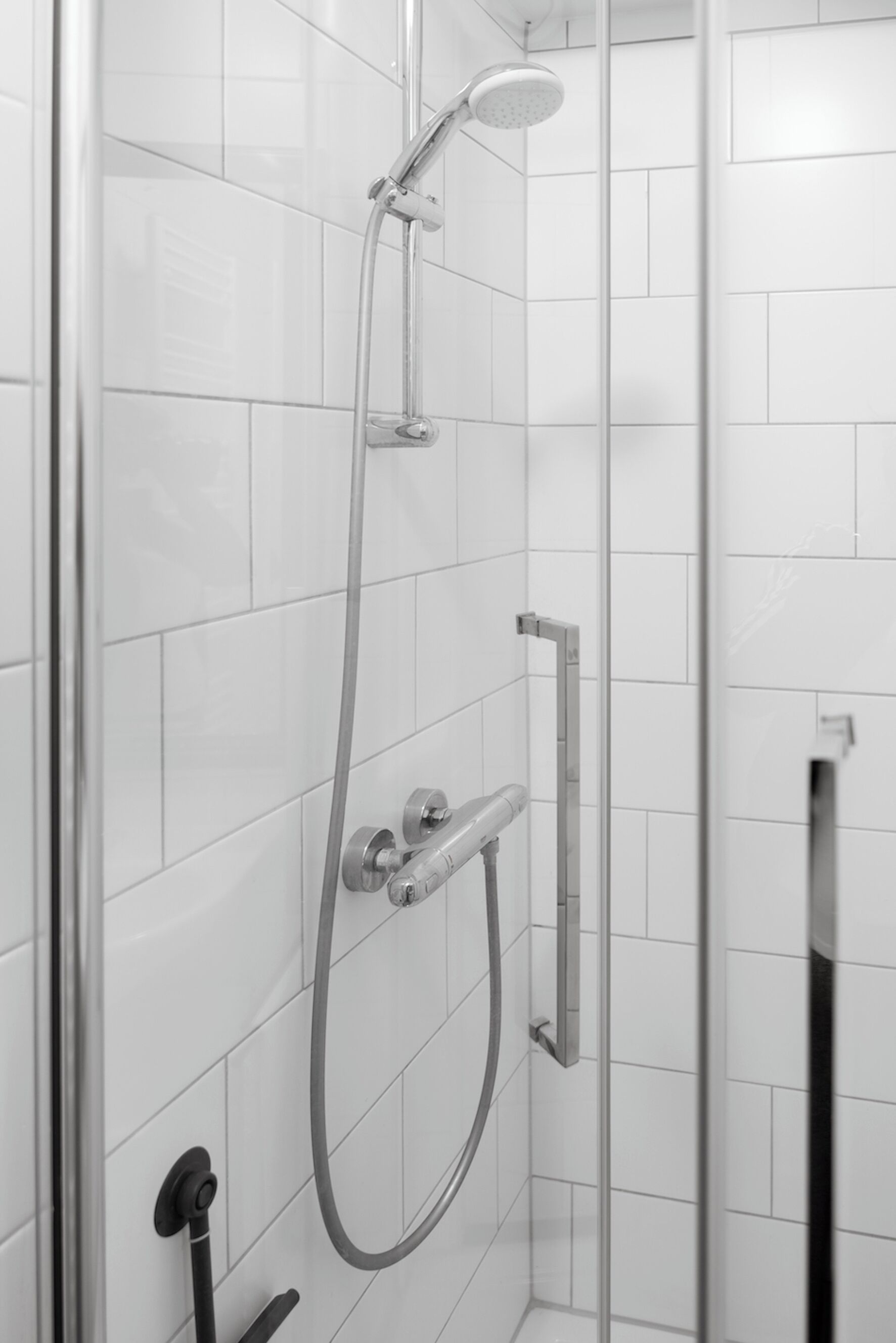 Une douche moderne dotée d’un pommeau de douche à main et d’un pommeau de douche fixe fixé au mur, tous deux avec des finitions chromées.