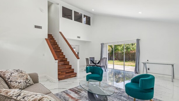 Ein geräumiges Wohnzimmer mit moderner Treppe, einem Glastisch und smaragdgrünen Sesseln.