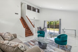 A spacious living room with a modern staircase, a glass coffee table, and teal armchairs. - Spacious 3BR Villa in Miami with Fenced Backyard (Miami)