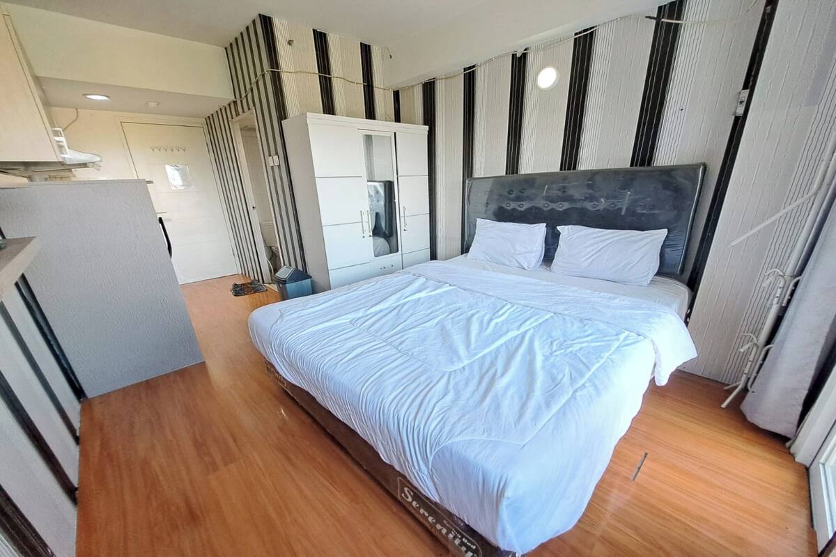A modern bedroom with a large bed, a wardrobe, and a kitchenette area.