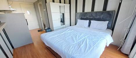 A modern bedroom with a large bed, a wardrobe, and a kitchenette area.
