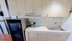 A compact kitchen with light wood cabinets, a stainless steel sink, and a black refrigerator with floral designs. - Hotel O Apartement Sentraland By Helen Mangement (Karawang)