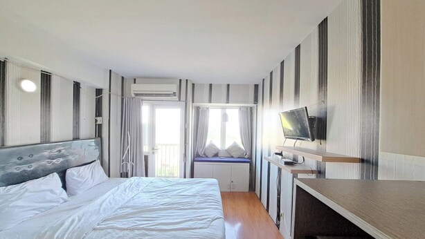 A hotel room with a bed, a TV, a window with curtains, and an air conditioning unit. - Hotel O Apartement Sentraland By Helen Mangement (Karawang)