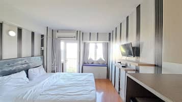 A hotel room with a bed, a TV, a window with curtains, and an air conditioning unit.