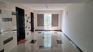 A hallway with a tiled floor, a door on the left, and a window with blinds on the right. - Hotel O Apartement Sentraland By Helen Mangement (Karawang)