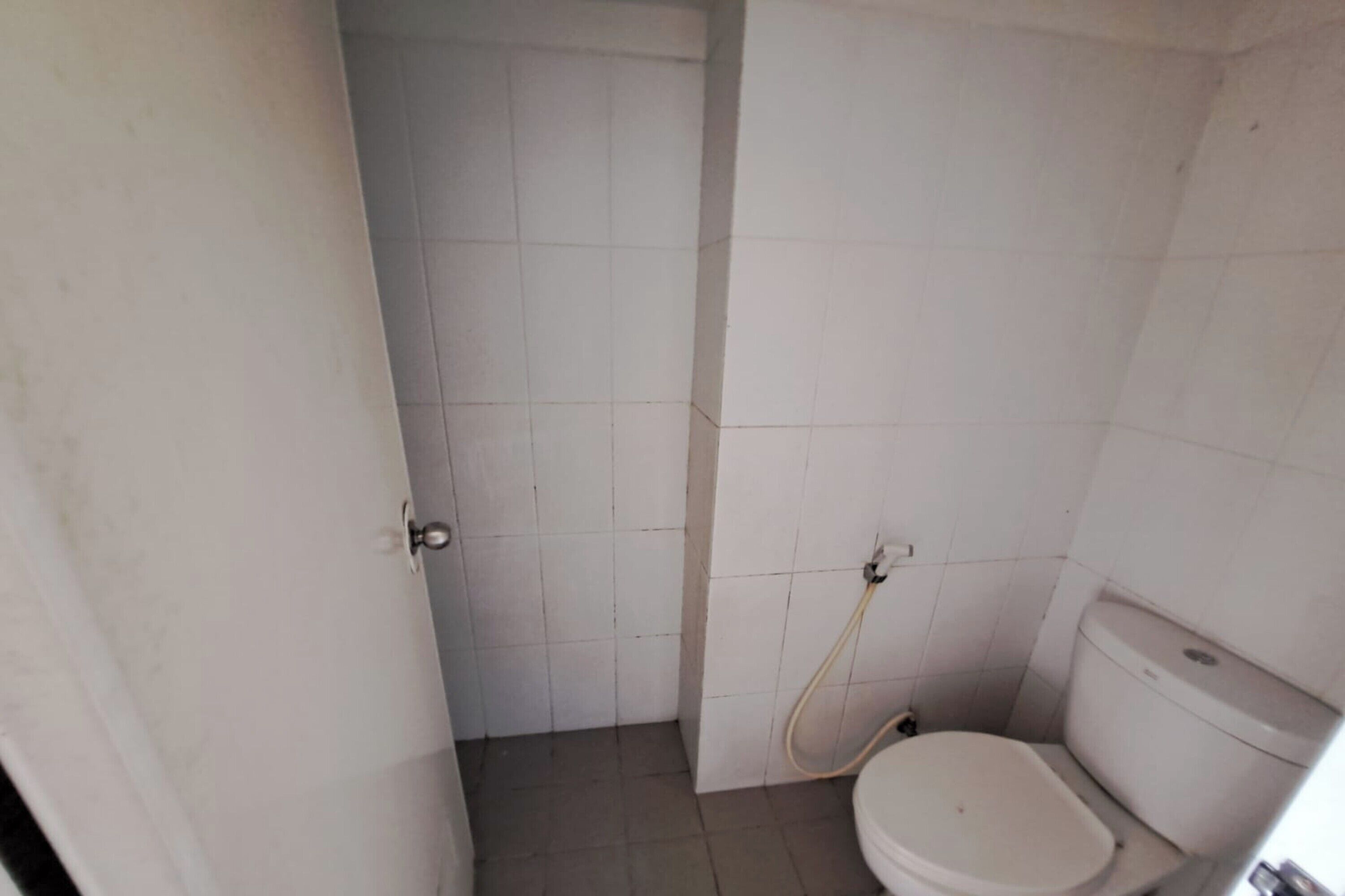 Une petite salle de bain carrelée, équipée de toilettes et d’une zone douche.