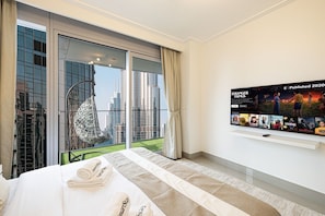 A hotel room with a large bed, a television mounted on the wall, and a view of the cityscape through the window.