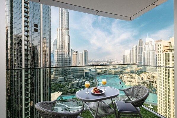 A balcony with a glass table, two chairs, and a view of a cityscape with high-rise buildings.