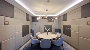 A modern conference room with a round table, six chairs, a vase with flowers, and a unique ceiling light fixture.