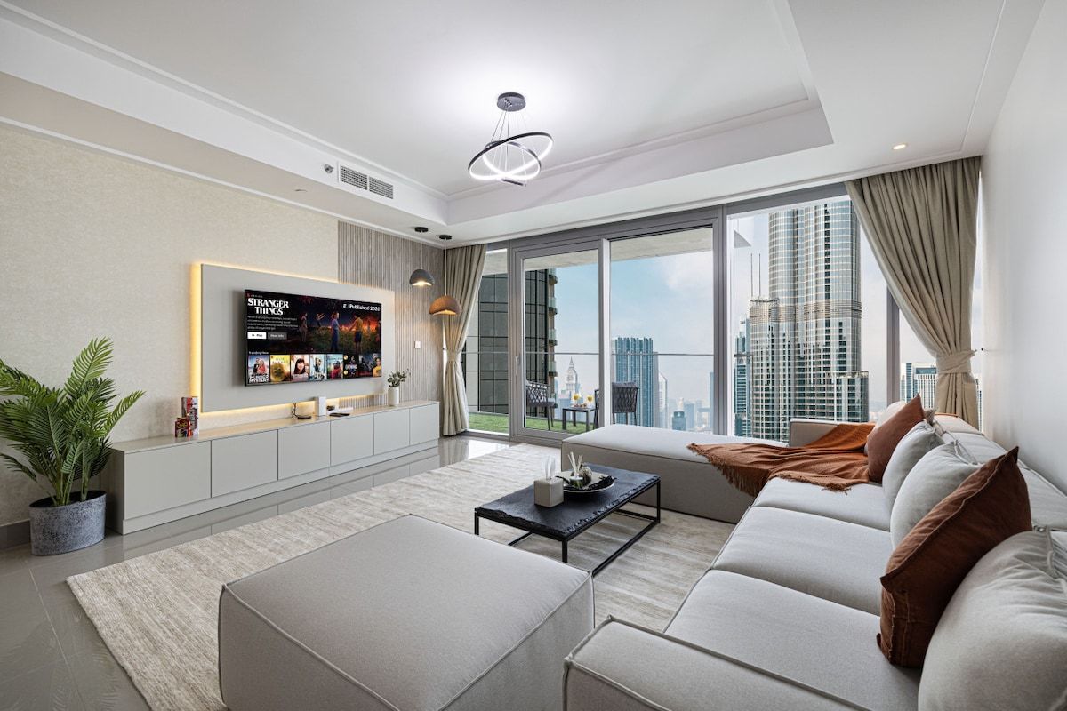 Een moderne woonkamer met een grote flatscreen-tv, een bank, een salontafel en een uitzicht op de stad door grote ramen.