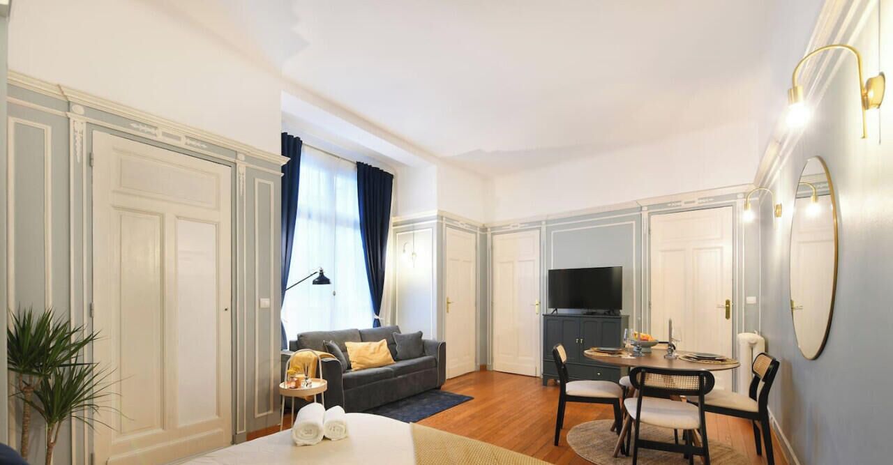 A hotel room with a sofa, dining table, chairs, a TV, and a bed.